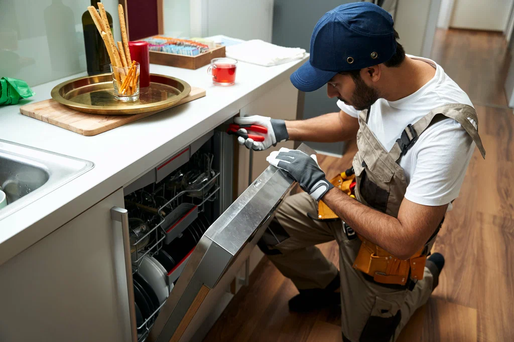 Friendly appliance repair technician smiling while repairing a fridge in a kitchen